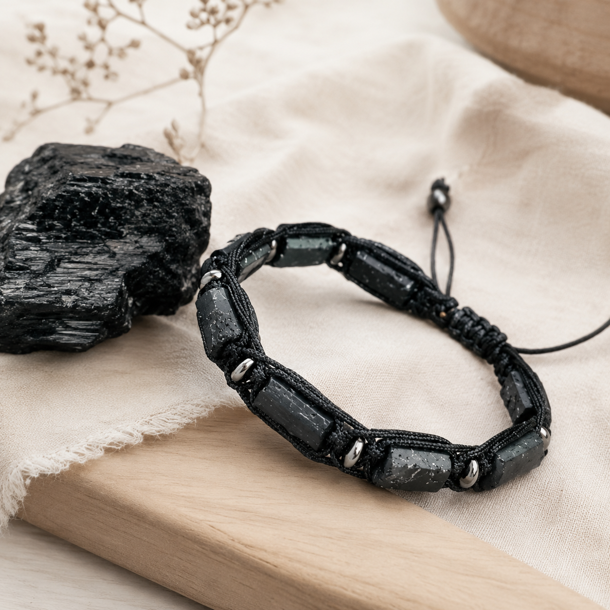 Tourmaline noire brute et bracelet posés sur du lin beige dans une composition sobre.