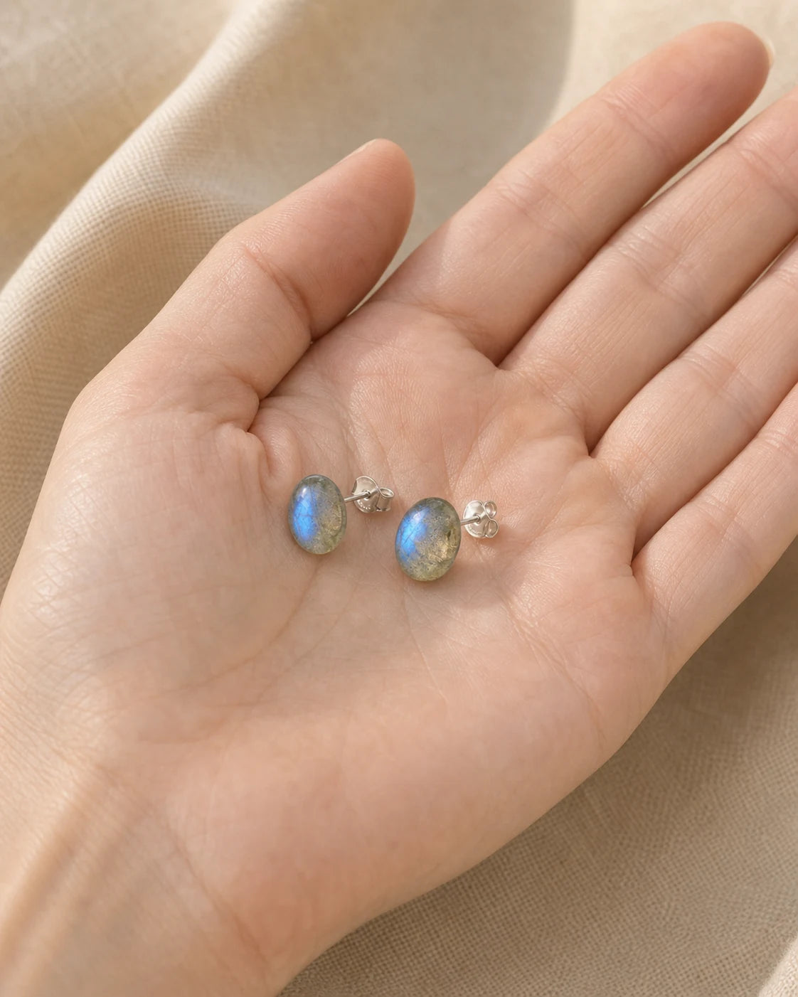 Paire de boucles d’oreilles à clous en labradorite présentée dans une main pour montrer son échelle