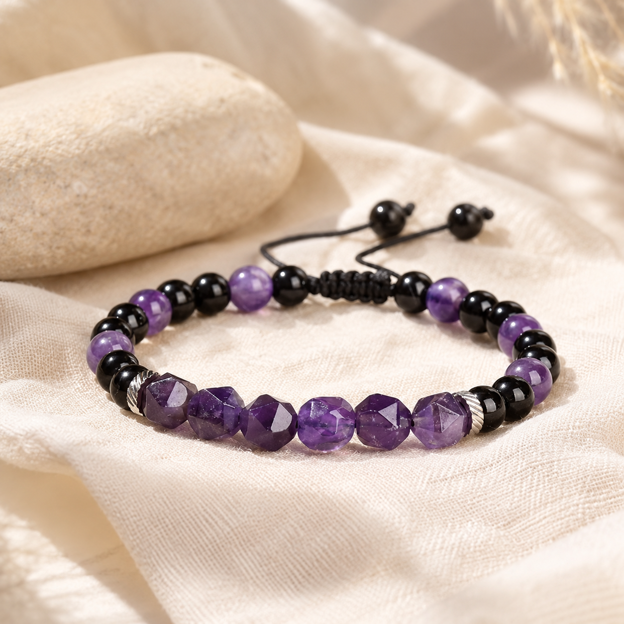 Bracelet en améthyste violette et onyx noir posé sur un tissu en lin beige naturel