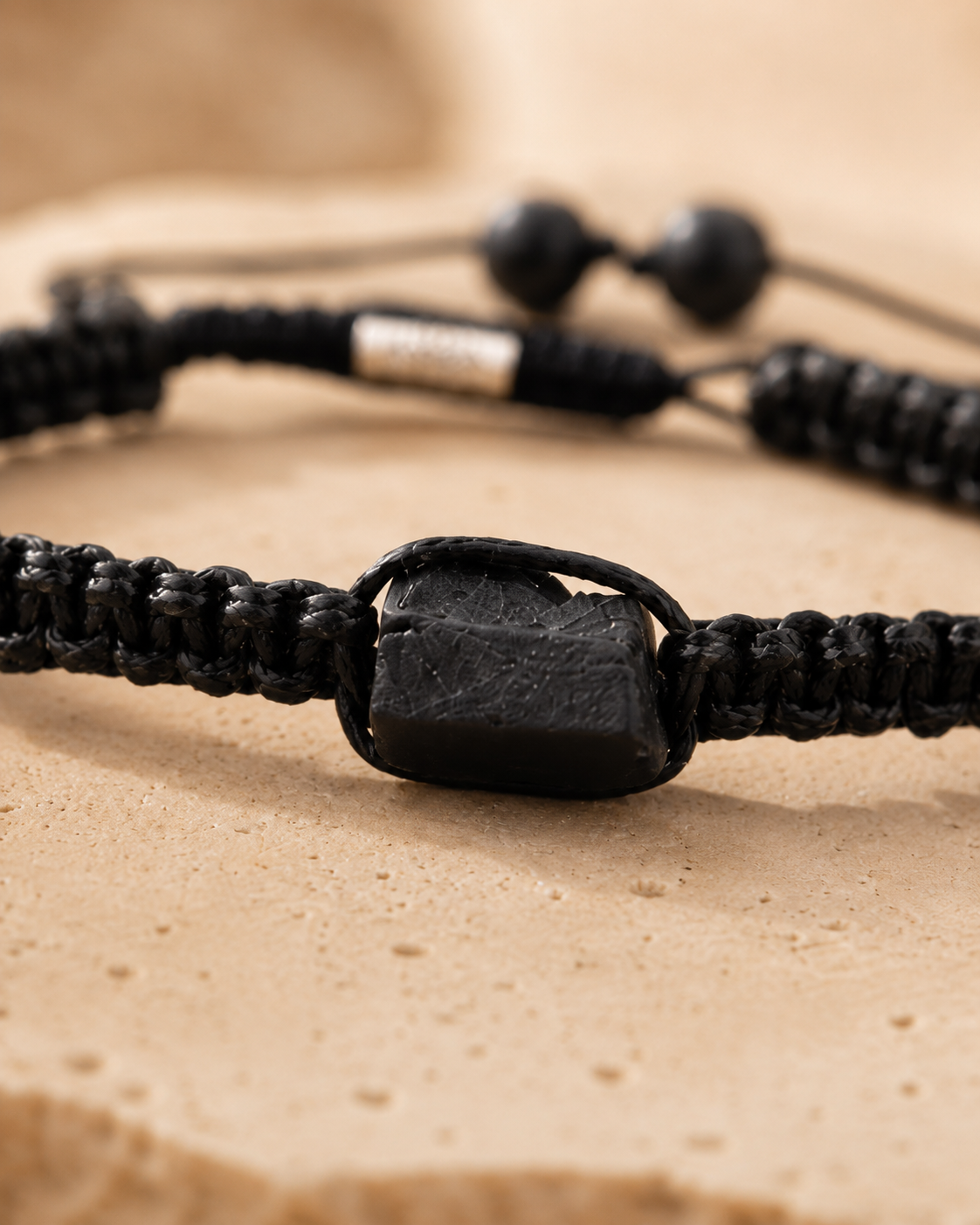 Gros plan sur la pierre brute noire et le tressage noir d’un bracelet minimaliste en tourmaline noire.