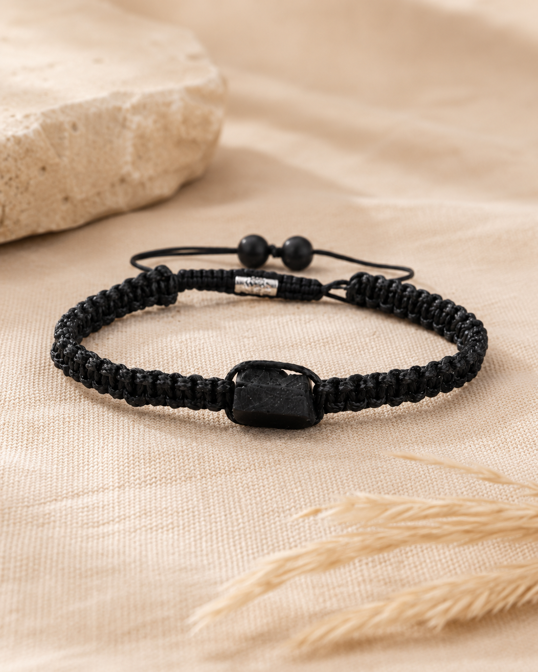 Bracelet minimaliste en tourmaline noire brute tressé, posé sur une pierre beige dans une ambiance naturelle.