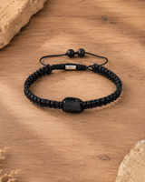 Vue complète d’un bracelet minimaliste en tourmaline noire brute tressé sur un fond en bois naturel.
