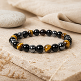 Bracelet œil de tigre, obsidienne et hématite dans une mise en scène rituelle sobre