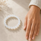 Bracelet en perles de pierre de lune blanche présenté près d’une main pour montrer son échelle.