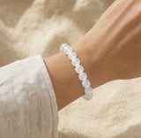 Bracelet en pierre de lune blanche porté au poignet avec une tenue claire.