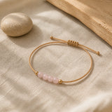Bracelet minimaliste en quartz rose posé sur du lin clair.