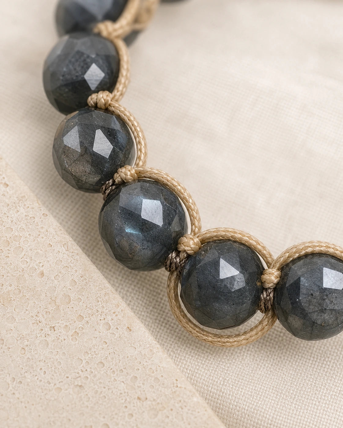 Gros plan sur les perles sombres en labradorite et le tressage beige