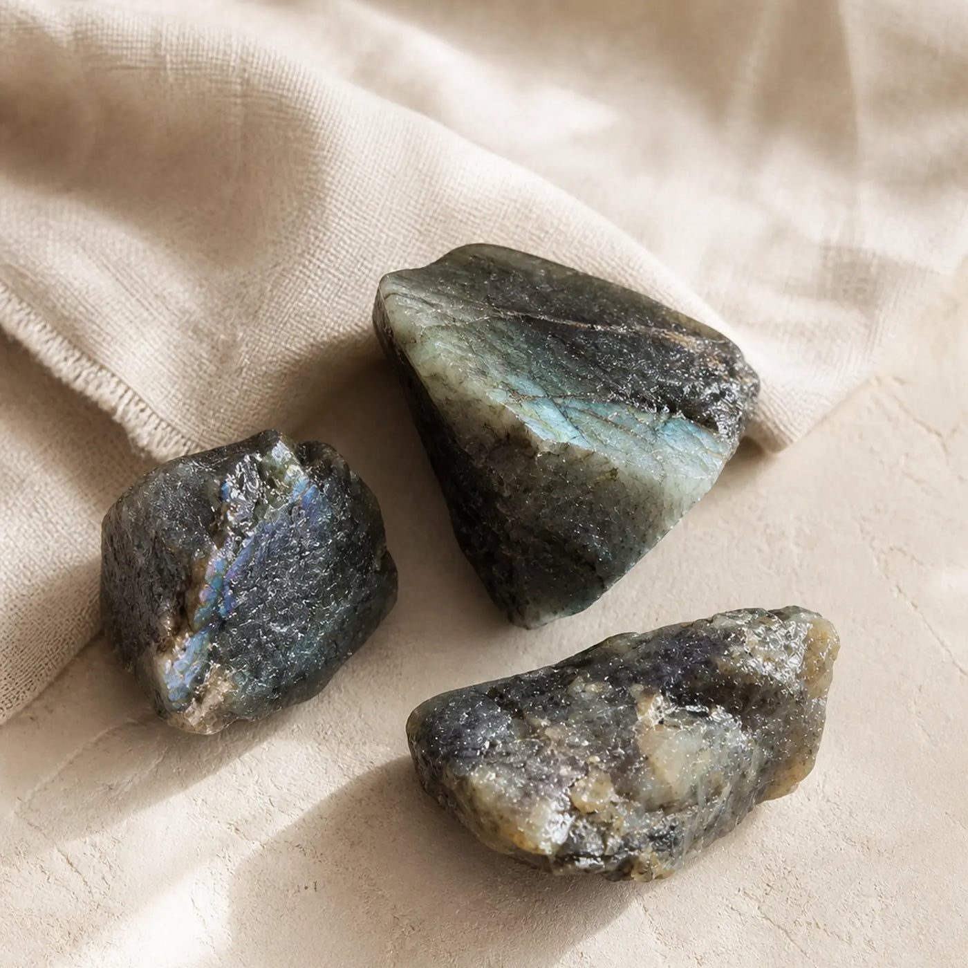 Lot de trois fragments de labradorite brute naturelle présenté sur du lin beige.