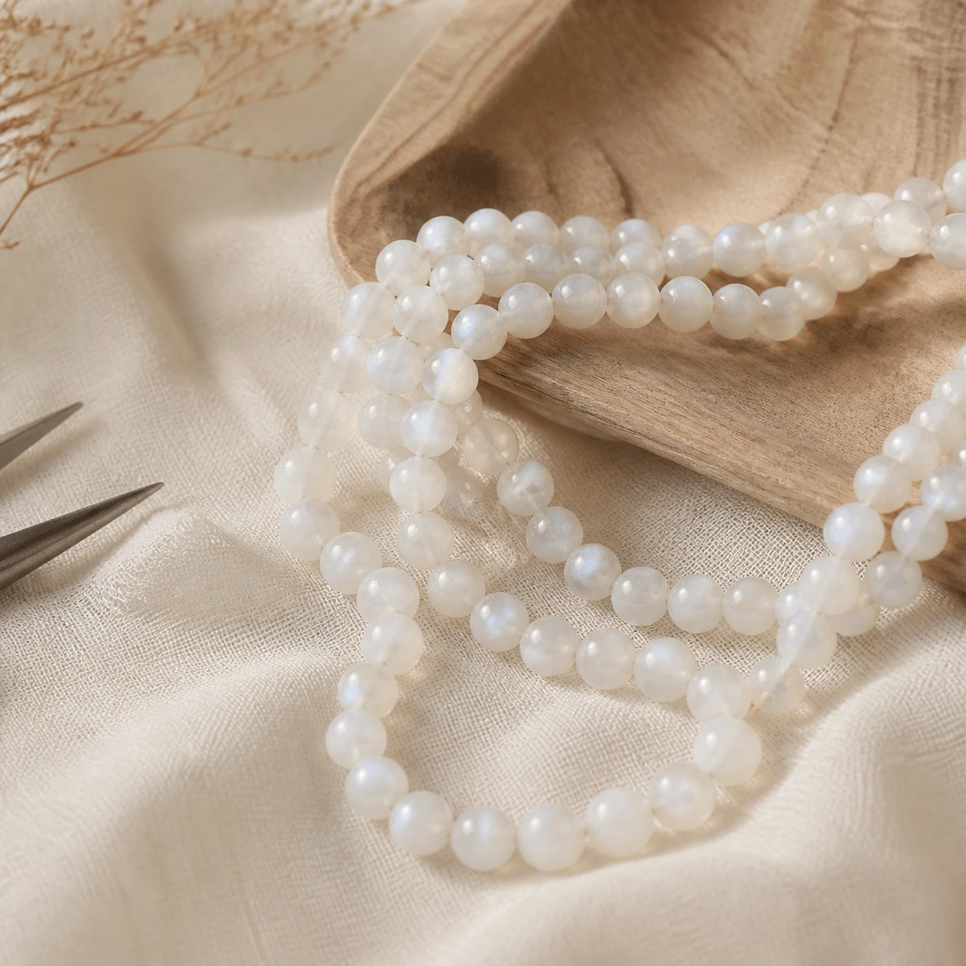 Fil de perles en pierre de lune blanche présenté sur du lin clair.