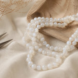 Fil de perles en pierre de lune blanche présenté sur du lin clair.