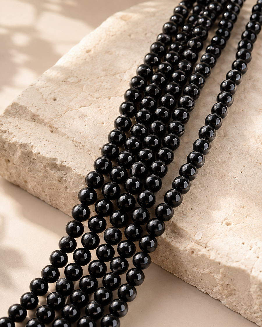 Perles de tourmaline noire naturelle pour création, présentées en plusieurs rangs sur une pierre beige.