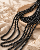 Plusieurs rangs de perles de tourmaline noire naturelle pour création mis en scène sur un plateau en bois et un décor minéral.