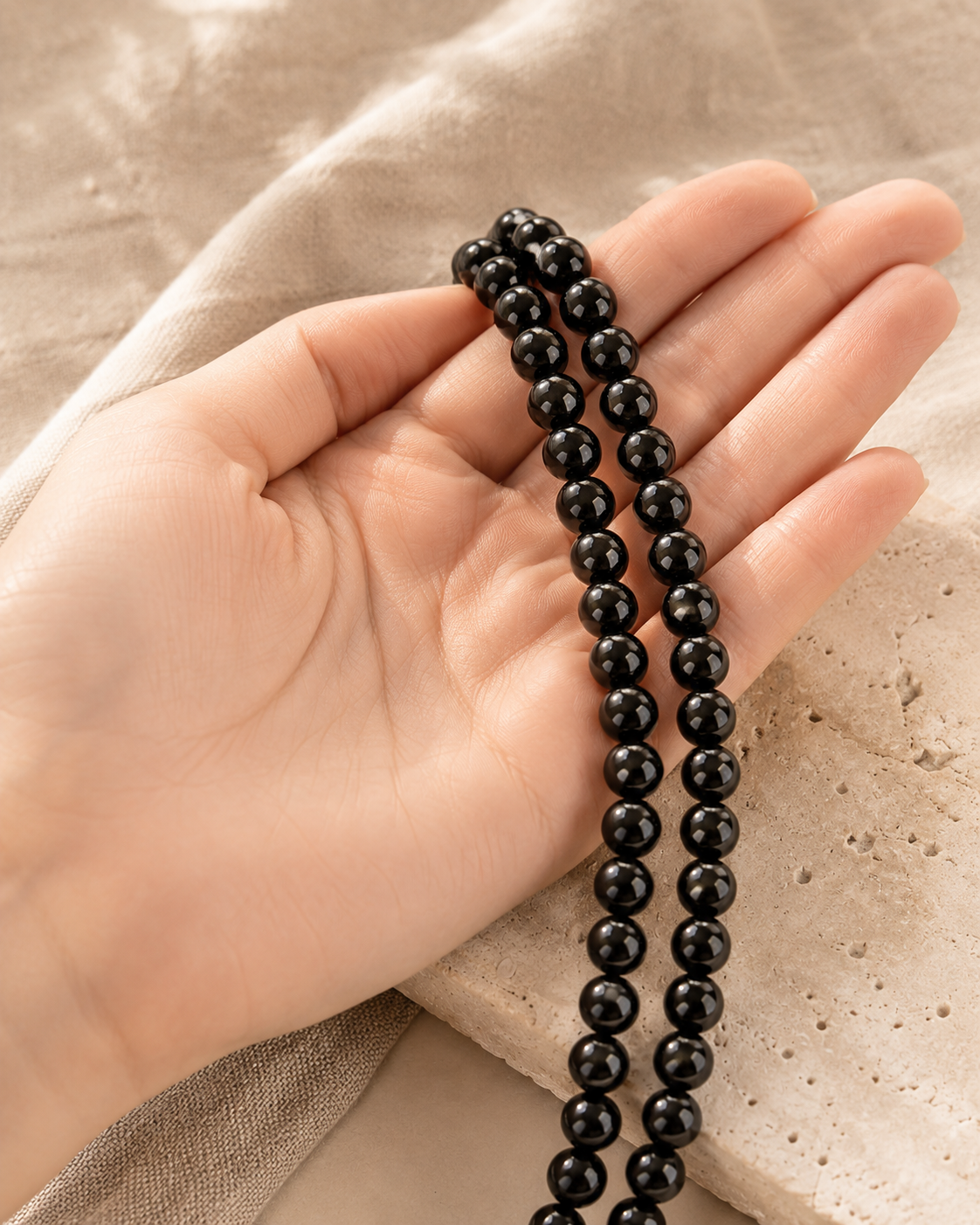 Deux rangs de perles de tourmaline noire naturelle tenus dans une main pour montrer leur taille.