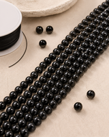 Perles de tourmaline noire naturelle pour création avec fil de montage et perles détachées sur fond beige.