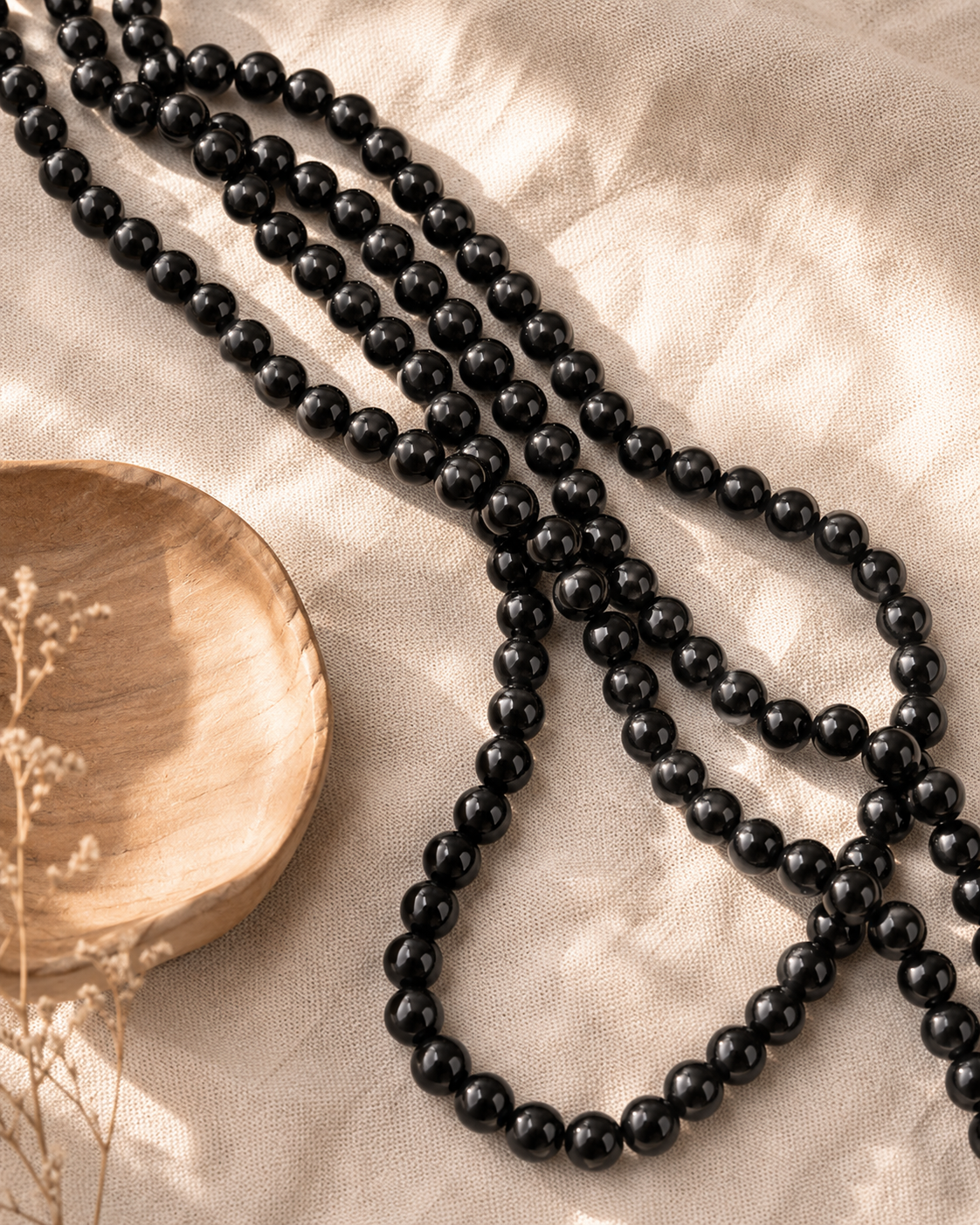 Rangs de perles de tourmaline noire naturelle pour création disposés sur un tissu beige près d’un bol en bois.