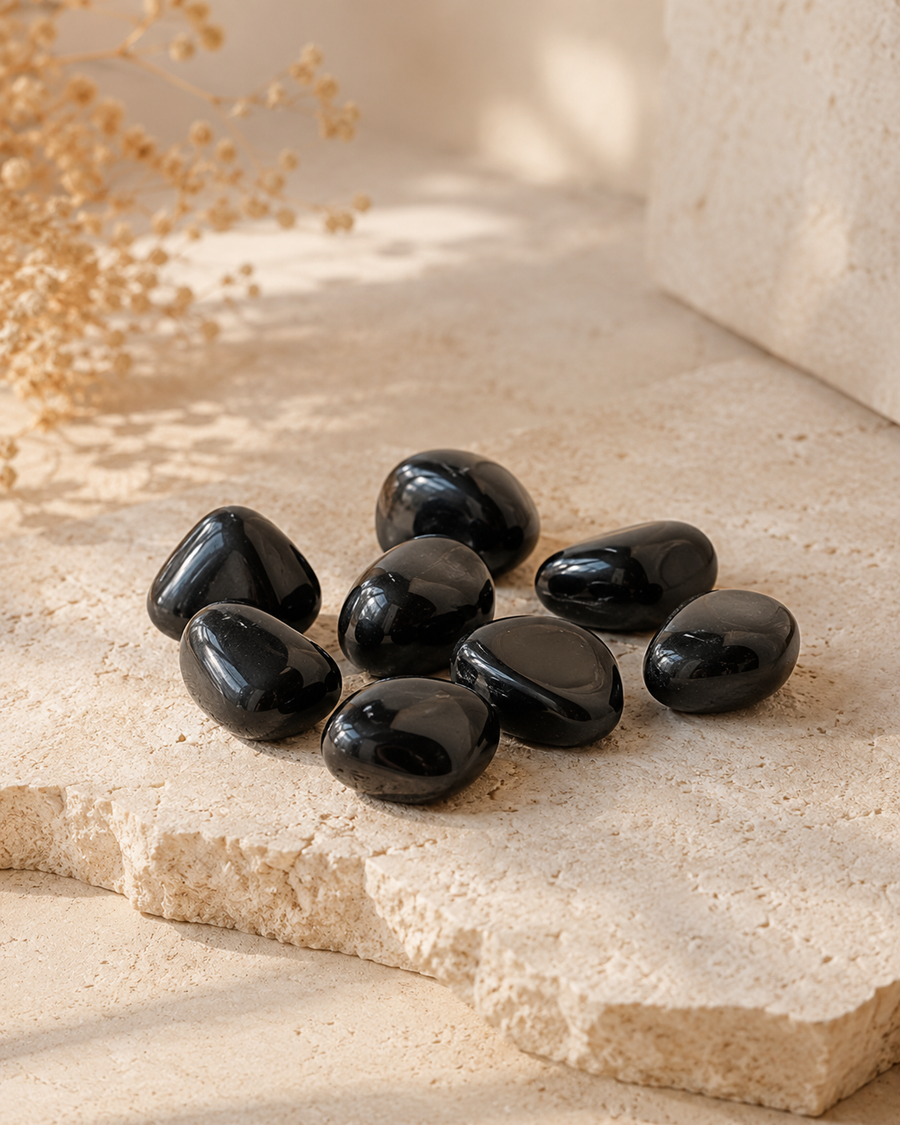 Pierres roulées de tourmaline noire naturelle posées sur une pierre beige dans une ambiance douce et minérale.