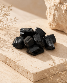 Tourmaline noire brute naturelle présentée en petit amas sur une pierre beige dans une ambiance minérale.