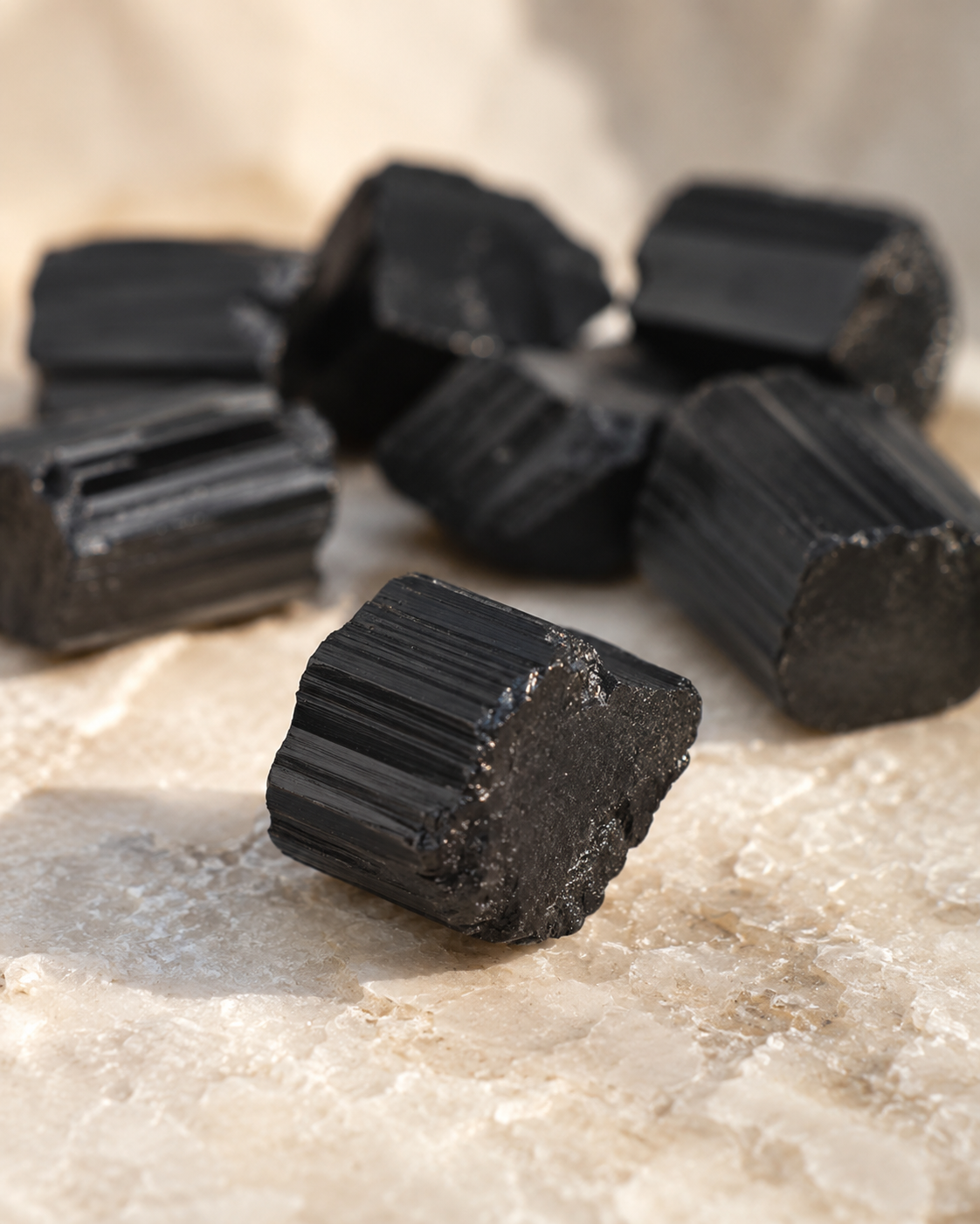 Morceau de tourmaline noire brute naturelle présenté en détail sur une surface minérale claire.