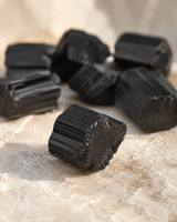 Morceau de tourmaline noire brute naturelle présenté en détail sur une surface minérale claire.